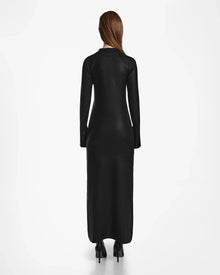 A woman with long, straight brown hair stands facing away, wearing the Rudsak FAIZA - 8524579 Black mock-neck maxi dress and black high-heeled shoes against a plain white background.