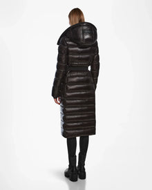 A person stands facing away, wearing the Rudsak FRIDA L-S - L124525 Black belted puffer coat with a hood, paired with black leggings and boots—an essential winter look—against a plain white background.