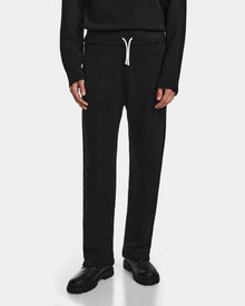 A person wearing Rudsak GEIGER - 9524512 Black M unisex knit lounge pants with a white drawstring, black shoes, and a black long-sleeve top stands against a white background. Only the lower half is shown.