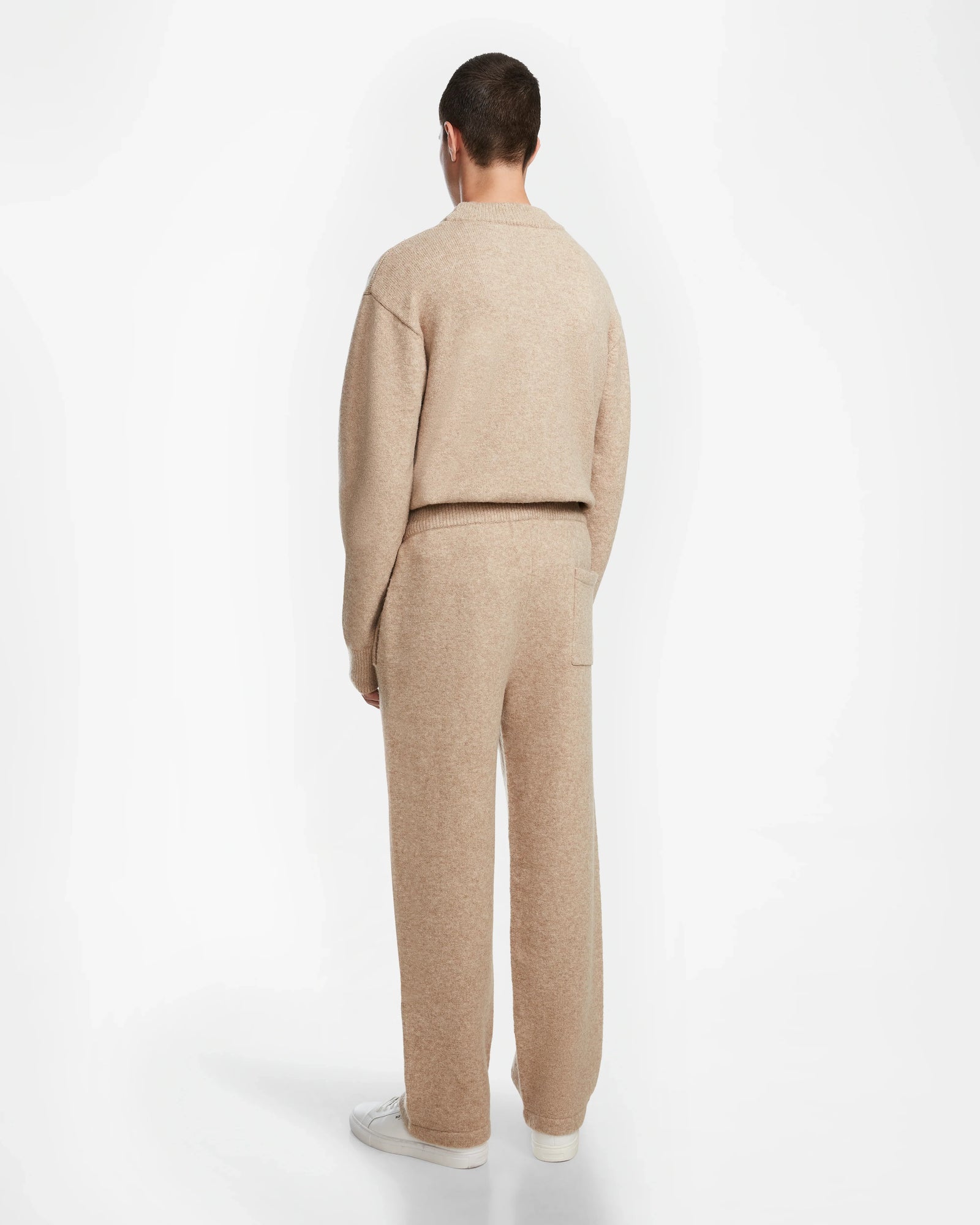 A person stands with their back to the camera, wearing the Rudsak GEIGER - 9524512 Camel M top and relaxed-fit lounge pants with white sneakers, against a plain white background.
