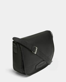 The GRAYSON - 8324512 Black crossbody bag by Rudsak features a flap closure, embossed front branding, and an adjustable shoulder strap, showcased against a plain light background.