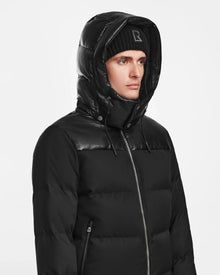 A person wears the Rudsak JACK - M124507 Black quilted jacket with hood and a black beanie, looking to the side against a plain white background.