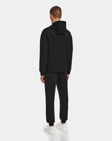 A man stands facing away, wearing the black Rudsak JARED - 6524533 hoodie and matching sweatpants with white sneakers, set against a plain light gray background.