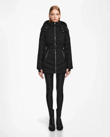 A woman faces forward against a white background wearing the Rudsak MALAYA M - L123554 Black women’s down puffer jacket with a hood, belted waist, and herringbone quilting, paired with black leggings and ankle boots.