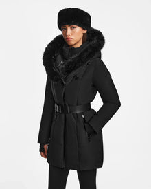 A woman wearing the Rudsak MODA M - 8124555 Black fur-trimmed winter coat and matching black leggings stands against a plain white background, looking directly at the camera with a neutral expression.