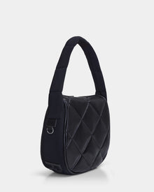 The NIOBE L - 8324503 Black by Rudsak is a black quilted shoulder bag with diamond-pattern stitching, a padded strap, soft structured shape, and a small metal ring detail, displayed on a plain white background.