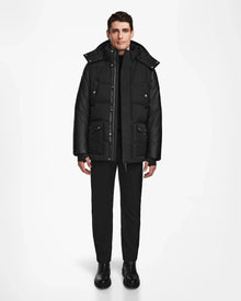 A man stands against a plain white background wearing the Rudsak RICKY R - M123506 Black men's quilted down parka with recycled leather sleeves, paired with black pants and boots. He faces forward, arms relaxed at his sides.