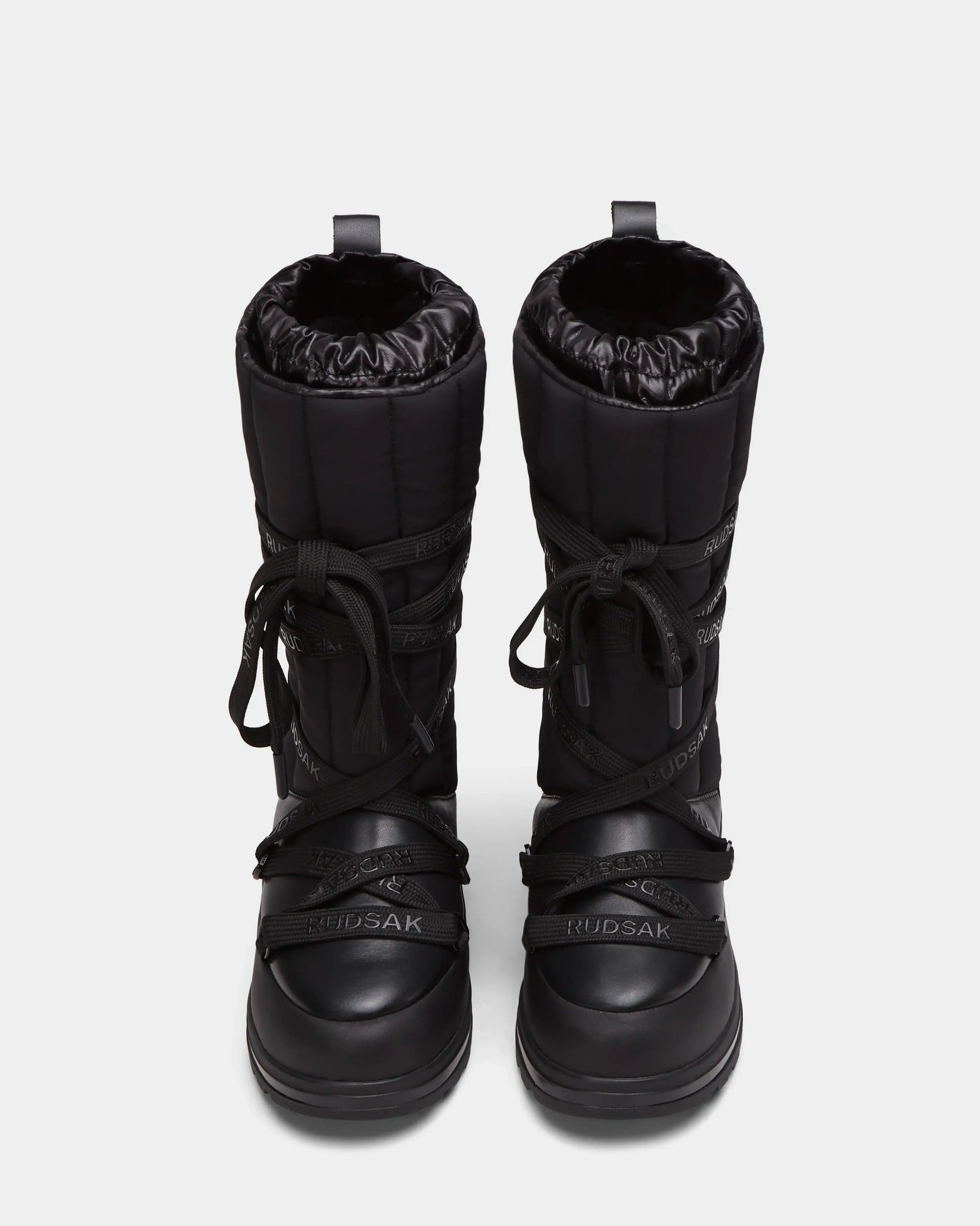 The RODIN - 8224502 Black womens winter boots by Rudsak feature thick anti-slip soles, a quilted upper, crisscross laces, and the Rudsak logo embossed on the front. Shown from a top-down view.