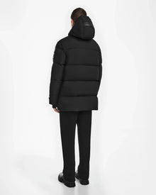 A person faces away from the camera, wearing the Rudsak ROKO - 6124510 Black mens quilted down parka with RDS-certified insulation, paired with black pants and shoes, set against a plain white background.