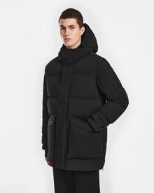 A person with short dark hair wears the Rudsak ROKO - 6124510 Black mens quilted down parka with RDS-certified insulation. Buttoned up with large pockets, they stand against a white background and look forward neutrally.