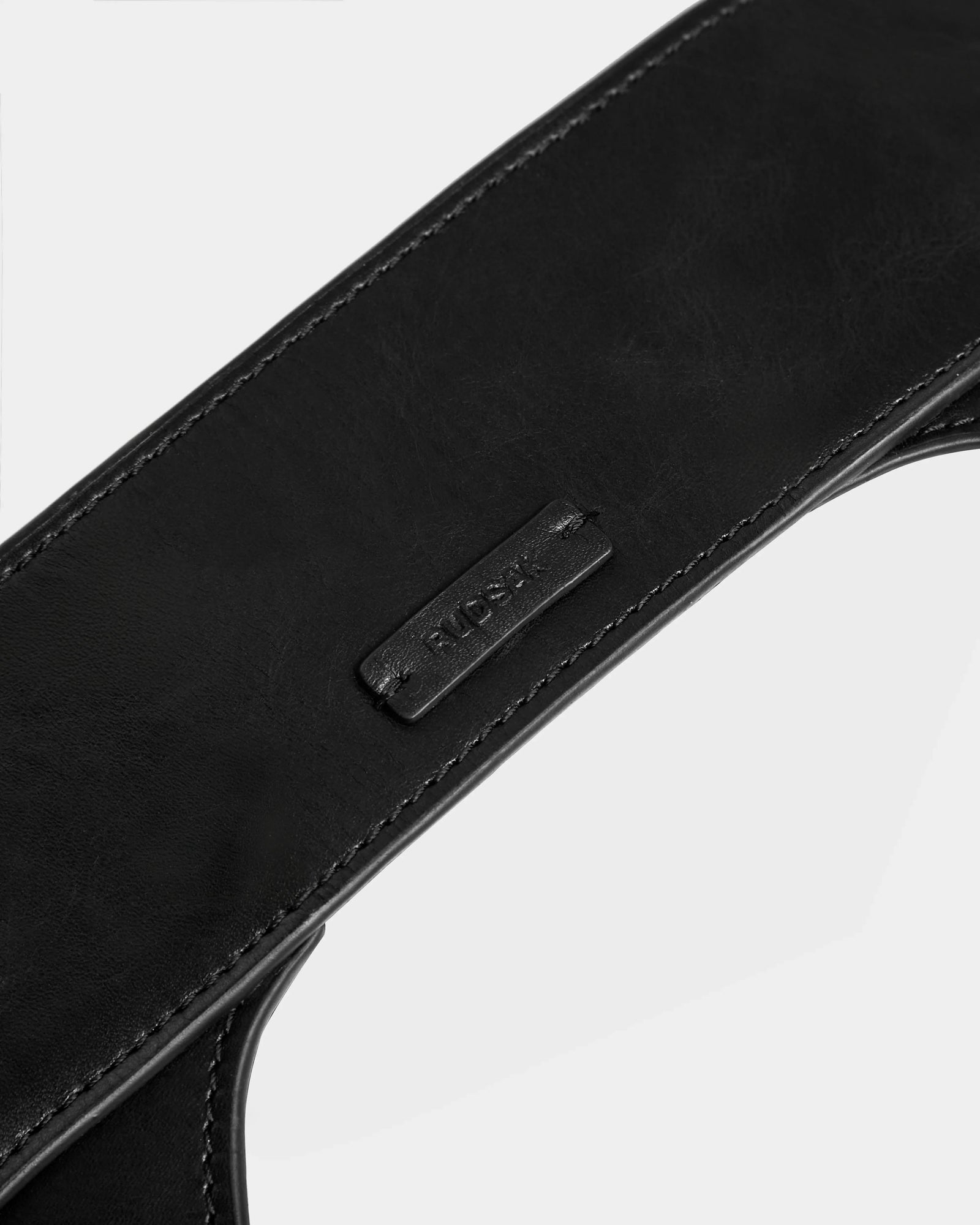 Close-up of a black womens leather waist belt, SIMONA - 8424522 Black by Rudsak, with neat stitching and a small rectangular patch embossed with the brand name. Set against a plain white background.