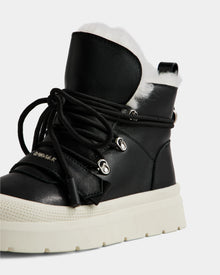 A close-up of the Rudsak ALEXEY L - L225518 Black women’s leather winter boot featuring a thick white sole, silver eyelets, black laces, and plush white faux fur lining visible at the top.