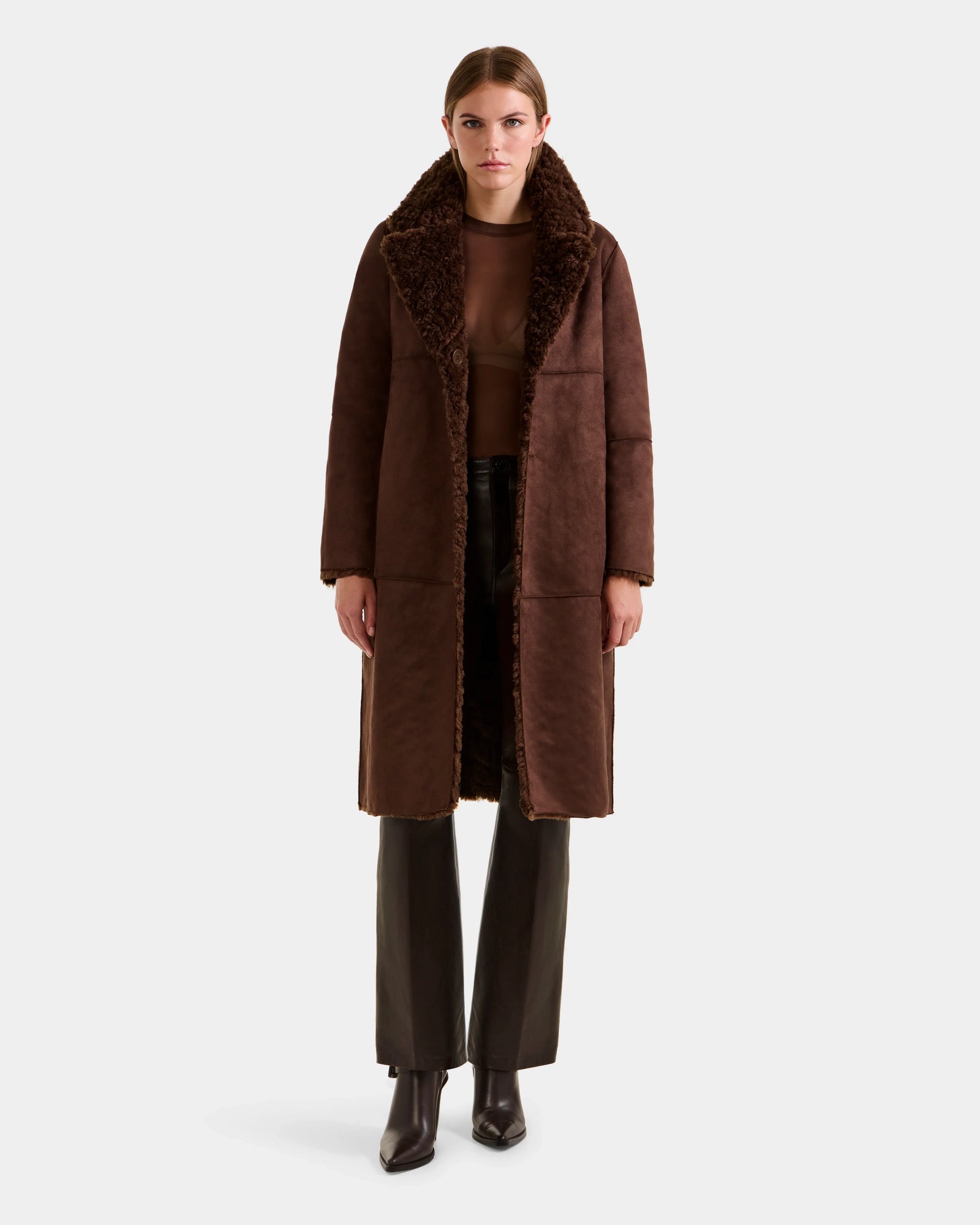 A woman faces forward against a white background, wearing the Rudsak ANNABELLE FSU - L125512 Espresso long brown sherpa teddy coat with a large collar over a brown top, black pants, and black heeled boots.