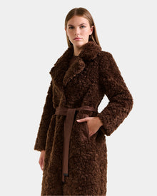 A woman with straight brown hair and a neutral expression models the Rudsak ANNABELLE FSU - L125512 Espresso sherpa teddy coat, featuring a wide collar and matching belt, against a plain light grey background.