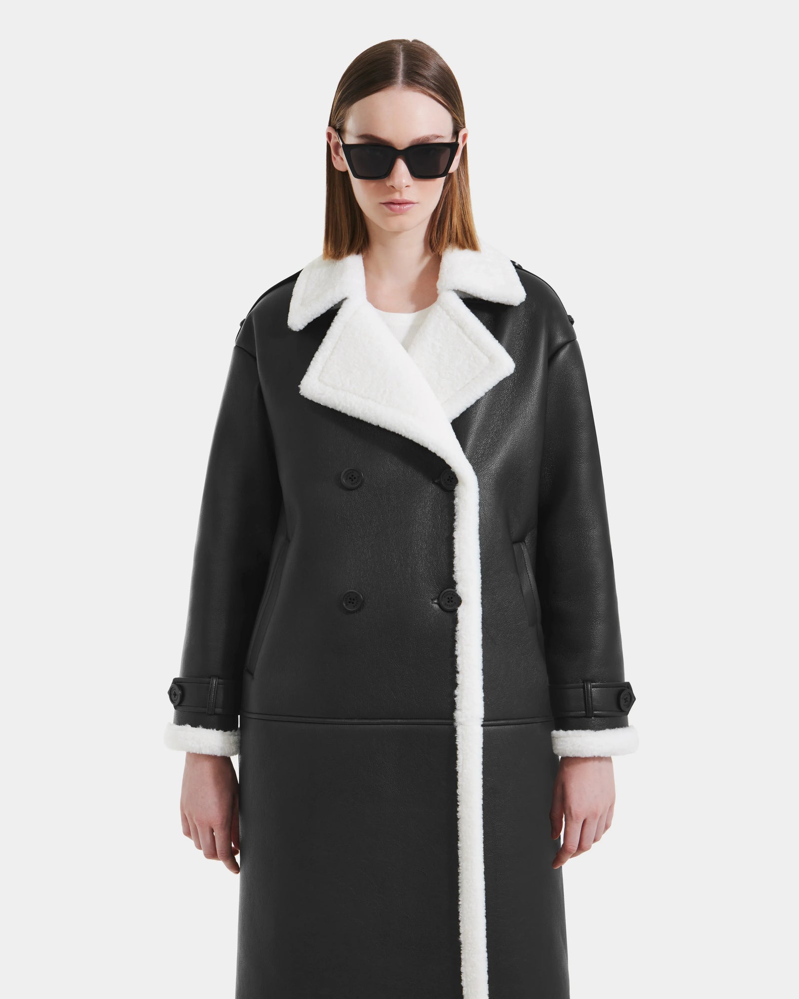 A person models the Rudsak DARCY - L125539 Black women's faux sherpa coat with white trim, standing against a plain white background and looking straight ahead with a neutral expression.