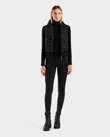 A woman faces forward wearing the Rudsak EMILY - L125515 Black hooded down bomber with a black turtleneck, leggings, and lace-up boots against a plain light gray background.