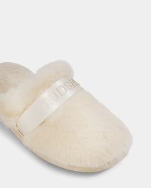 A close-up of the FLUFF - L223509 Cream women's slipper by Rudsak, featuring cream-colored faux fur and a wide shiny band with embossed RUDSAK text, set against a plain white background for a cozy lounge look.