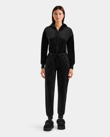 A woman faces forward wearing the Rudsak KETZY - L525503 Black women’s velour hooded jumper with long sleeves, elastic waist, and matching black slippers, set against a plain light gray background.