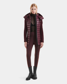 A woman stands facing forward wearing the Rudsak MARRY S - L125521 Wine weather-resistant puffer vest, a sheer black top, burgundy fitted pants, and black ankle boots against a plain white background.