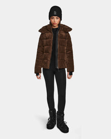 A woman faces forward against a white background, wearing the Rudsak MIRRY FF - L124507 Espresso women’s short down puffer jacket, black leggings, black winter boots, and a black beanie with a white 