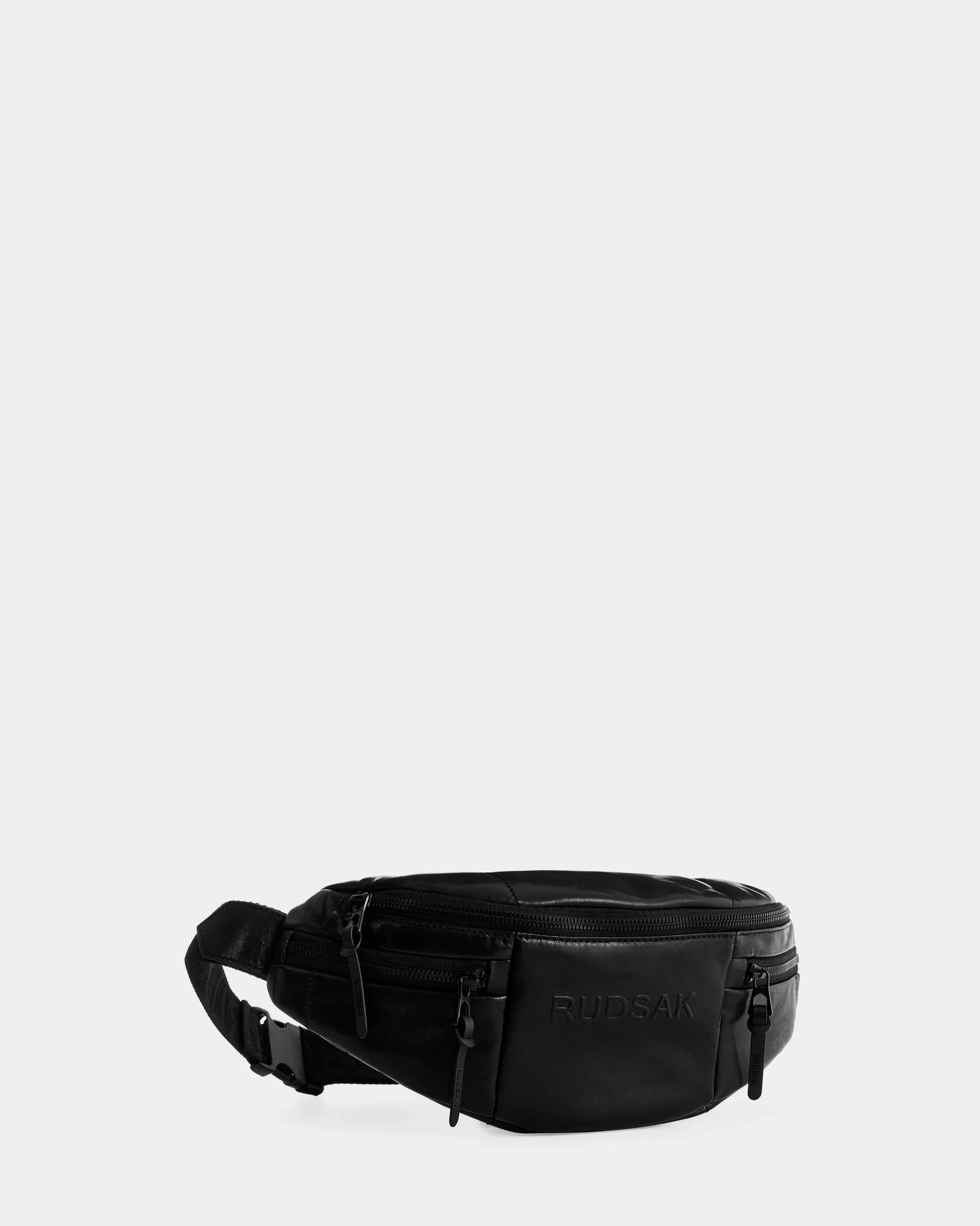 The RILONI L - U325002 Black by Rudsak is a unisex leather belt bag with multiple zippered compartments, an adjustable strap, and embossed branding on the front, shown against a plain light gray background.