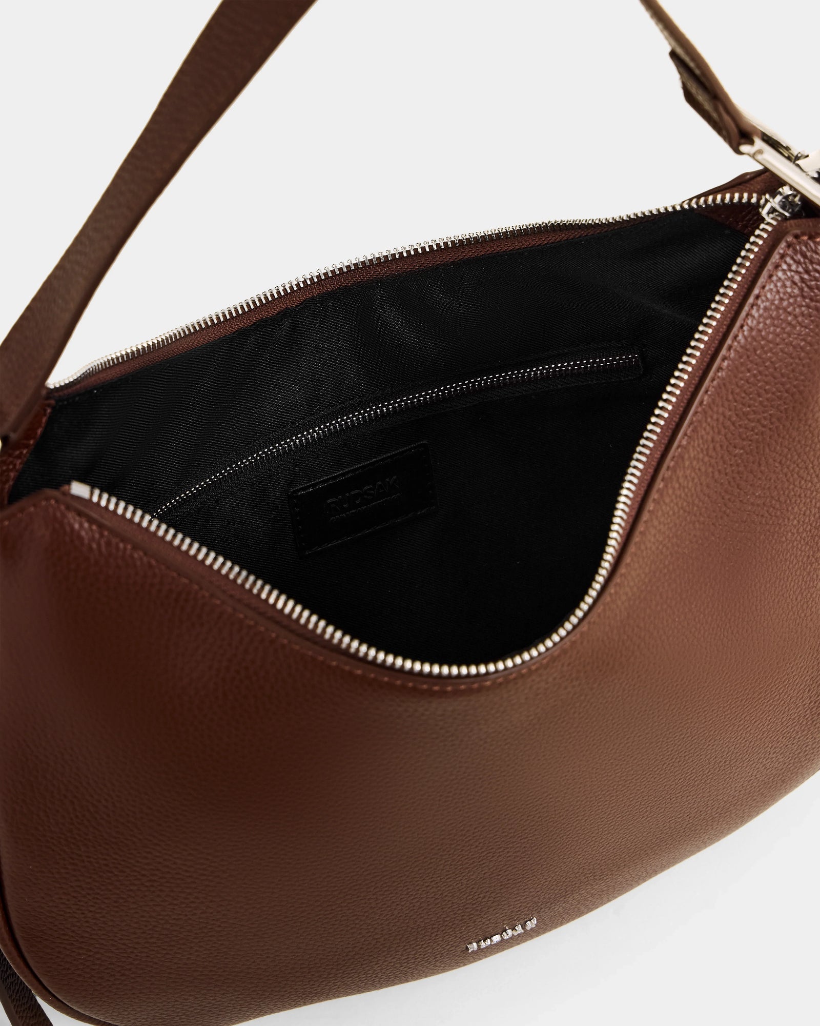 A close-up of the Rudsak SYLVIA - L325515 Mocha women’s leather shoulder bag features an open brown design with a silver zipper, black fabric lining, and an inner zippered pocket.