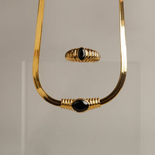Model. Gold necklace with black beads on a gray background