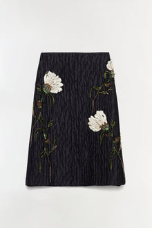 Black midi skirt with embroidered white flowers and green stems on textured jacquard fabric.