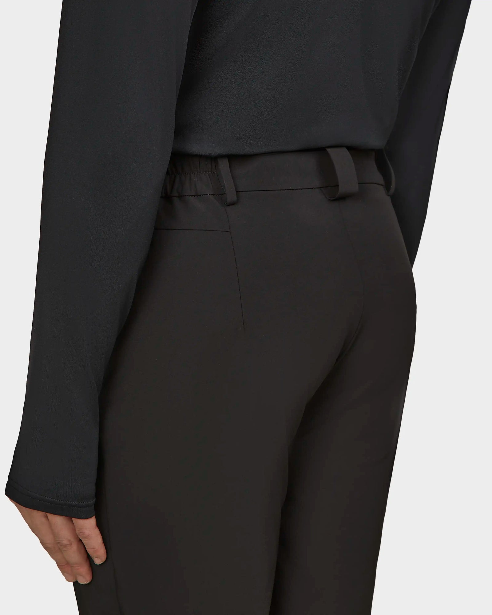 A person wearing Rudsak KICO - 6523508 Black tailored pants and a black long-sleeve top, seen from the back and waist down with one arm resting by their side.