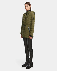 A woman wears the Rudsak FRANCINE - 8124722 Loden Green puffer jacket with black zipper details, paired with black leggings and boots, posed against a plain white background.
