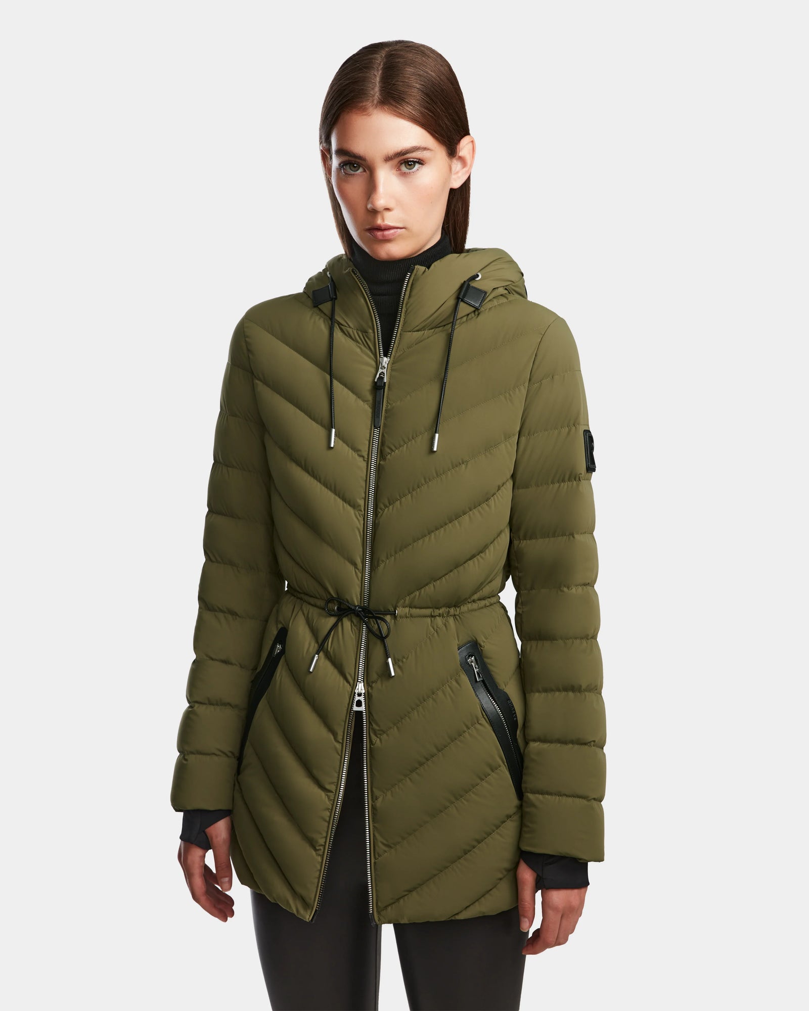 A woman wearing the Rudsak FRANCINE - 8124722 Loden Green light down puffer jacket with a drawstring waist and zippered pockets, standing against a plain white background.
