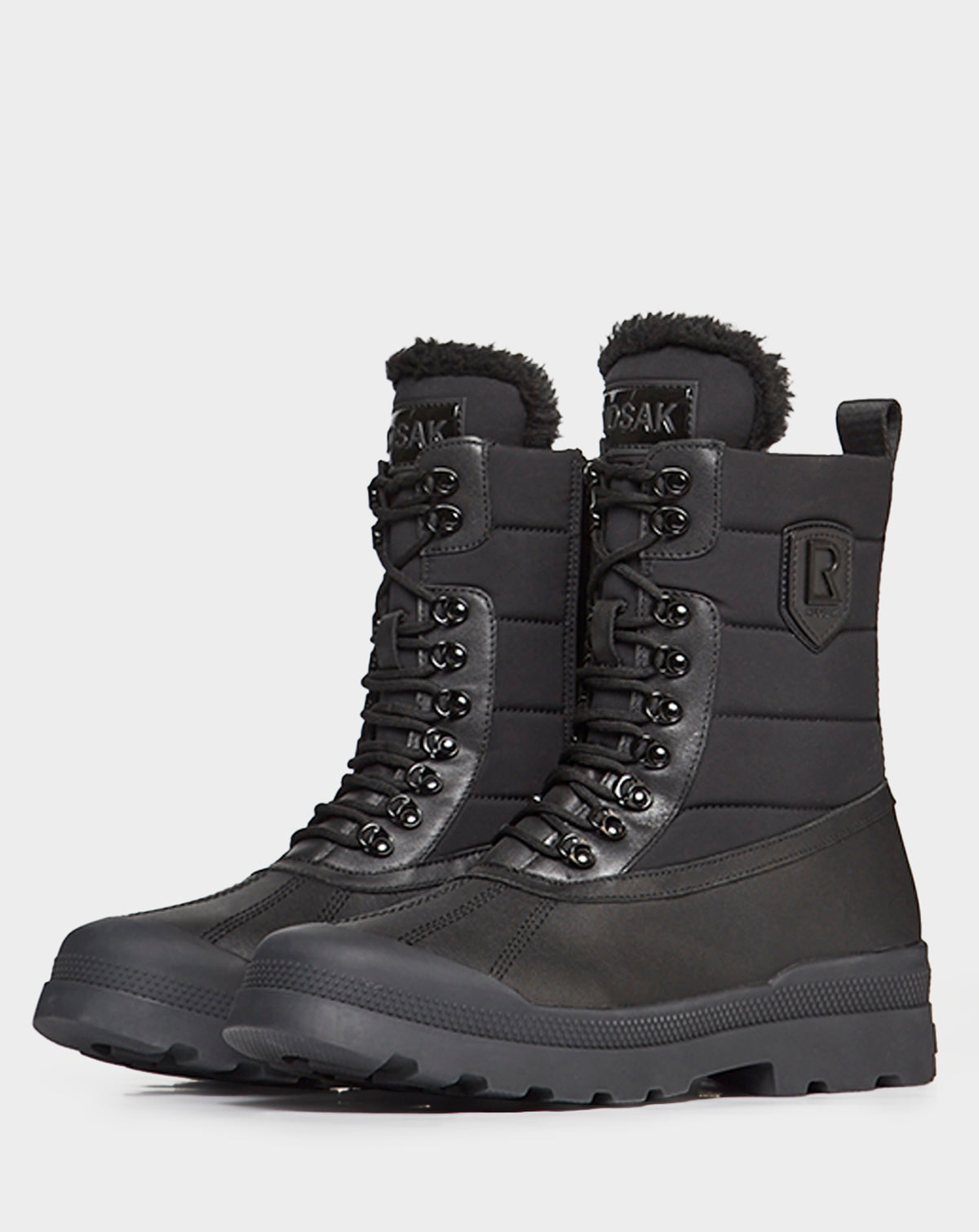 REAGAN - 6222500 BLACK by Rudsak: black high-top leather winter boots with thick rubber soles, lace-up fronts, padded shafts, and faux fur lining at the top, shown on a plain white background.