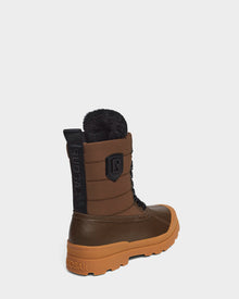 The Rudsak REAGAN - 6222500 Army is a mens winter boot in brown and tan with black laces, a rugged orange sole, fur-lined top, and the RUDSAK logo on the side. Made of leather and shown against a plain white background.