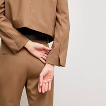 back image of a woman standing wearing the Neale jacket in camel