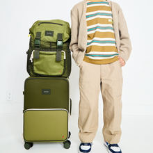 Boy standing with STATE Bags Grove Rucksack Olive and Logan Carry-On Suitcase Olive