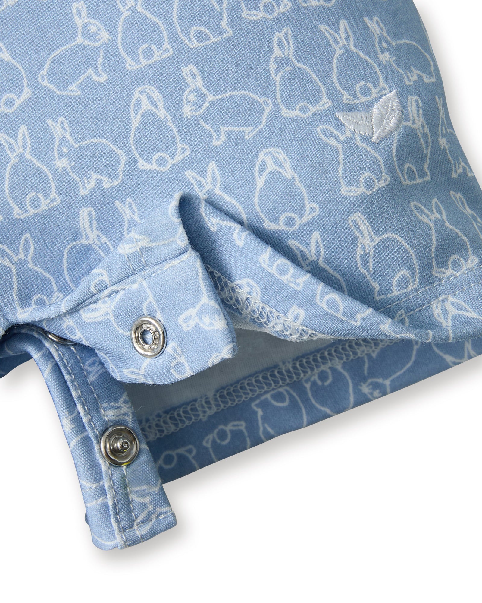 The Baby's Pima Louis Play Romper in Hoppy Days Blue is a light blue short-sleeve romper with a white collar and sleeve cuffs, a white bunny outline pattern, and bottom snaps for easy changing.