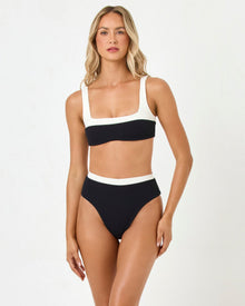 front view of woman wearing a black and white bikini on a plain background