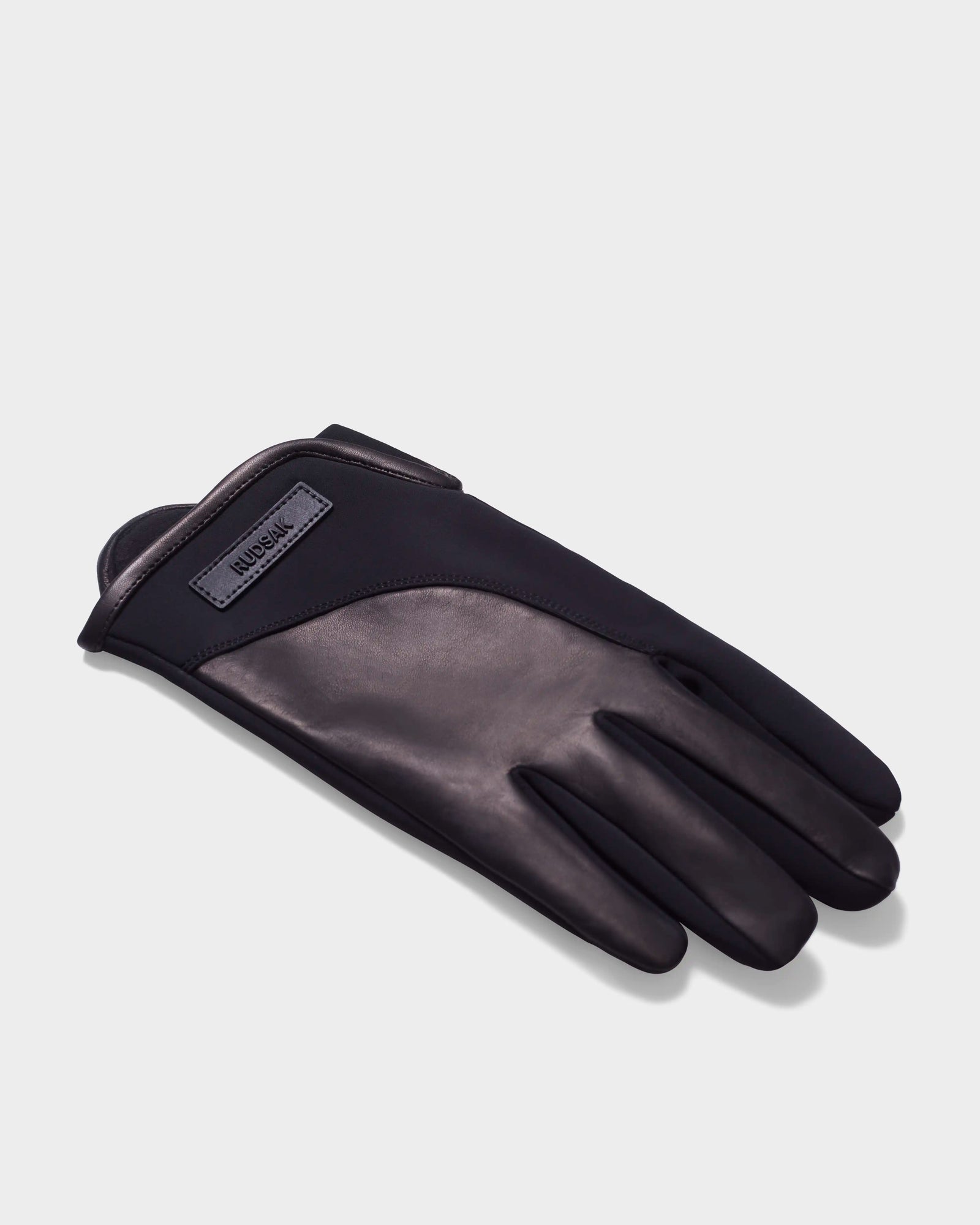 A single ERIK - 6423500 Black mens leather glove by Rudsak is laid flat on a light gray surface, featuring smooth leather, fabric trim, and a small rectangular Rudsak label near the wrist—ideal for stylish winter wear.