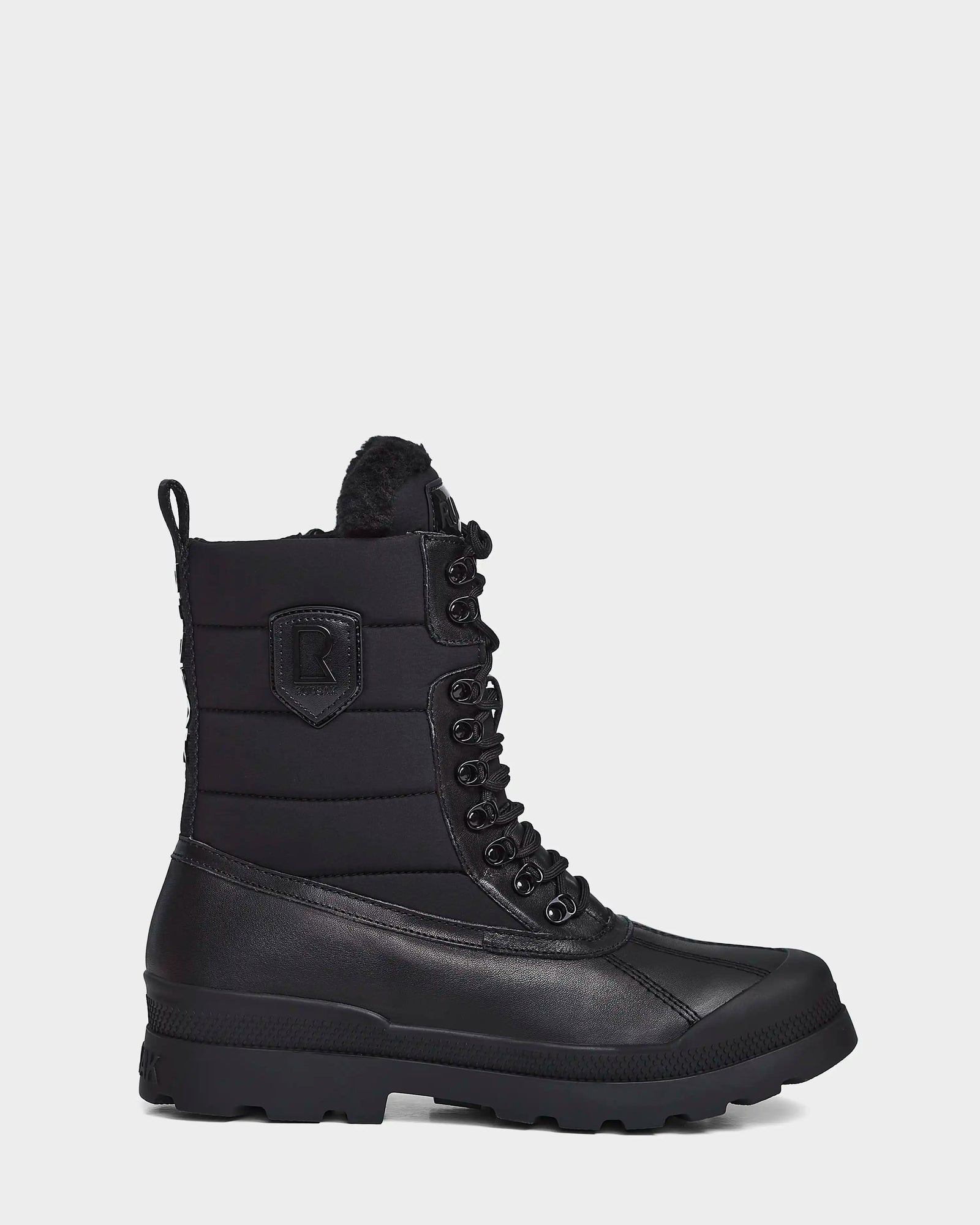 The REAGAN - 6222500 BLACK by Rudsak is a black mens mid-calf winter boot with a rugged rubber sole, padded upper, side patch detail, and faux fur lining at the top—crafted for warmth and style against a white background.