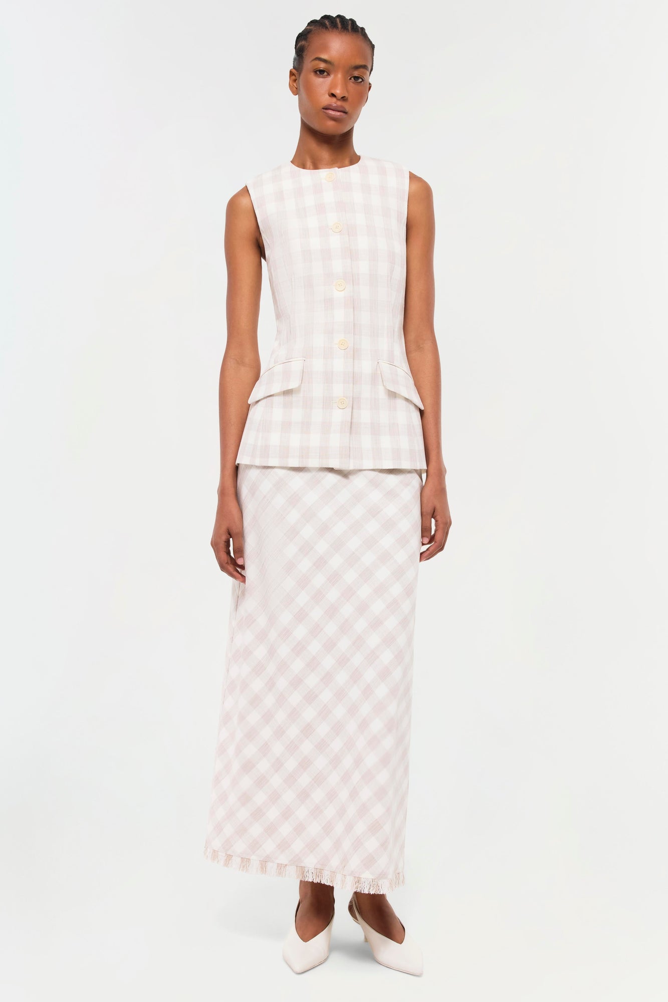 Woman wearing a sleeveless button-front vest in light pink and white gingham check with matching maxi skirt.