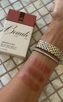 Arm with four pink lip-tint swatches and bracelets beside a Beauté lip tint box labeled Beauté; shades Guava, Paloma, Cocoa.