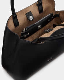 A close-up of the Rudsak CATIRA S - 8325006 Black women’s tote bag in black pebble leather with tan suede lining, featuring a zippered inner pocket, snap closures, sturdy handles, and a removable shoulder strap for versatility.