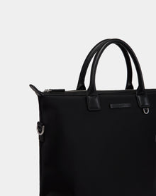 A close-up of the Rudsak DEXTER - 9324513 Black unisex tote bag with leather handles, silver hardware, and a zipper closure, set against a plain light gray background—a stylishly versatile accessory for any occasion.