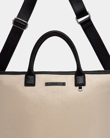 A close-up of the Rudsak DEXTER - 9324513 Vanilla tote bag features beige canvas, black leather handles, and a detachable black shoulder strap, highlighting this versatile accessory against a plain background.