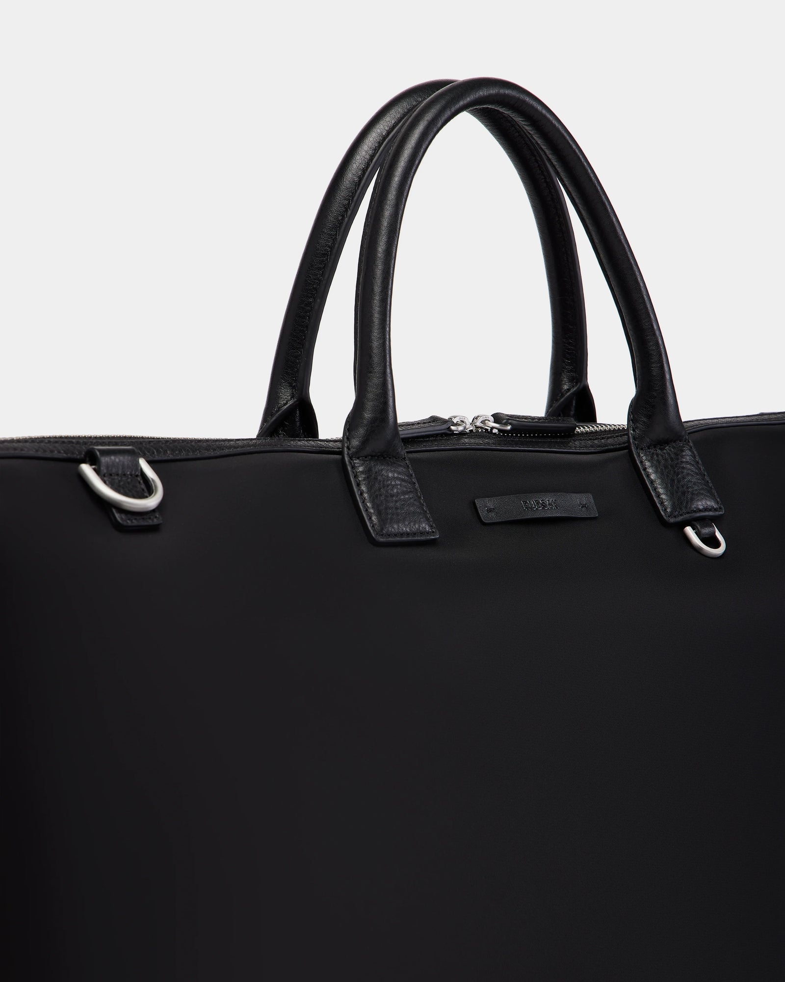A close-up of the Rudsak DUBLIN - 9324514 Black canvas leather bag with silver hardware, featuring two sturdy handles and a zippered top—ideal as a unisex travel bag, set against a plain light background.