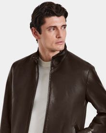 A man with short dark hair wears the Rudsak STEVEN - 6124541 Espresso leather jacket over a light shirt, glancing left against a plain background.