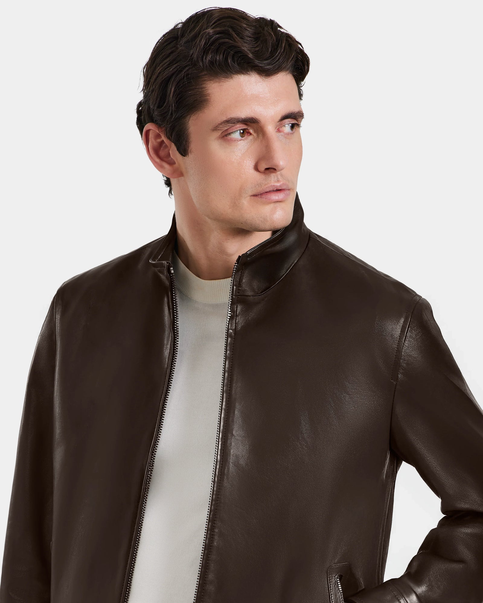 A man with short dark hair wears the Rudsak STEVEN - 6124541 Espresso leather jacket over a light shirt, glancing left against a plain background.