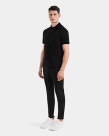 A man stands slightly turned in a WALTER - 6524531 Black/Black polo by Rudsak, black pants, and white sneakers against a plain light gray background.