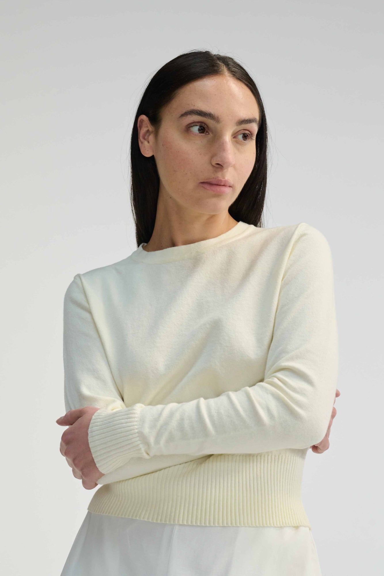 Woman wearing an ivory long sleeve sweater against a plain background