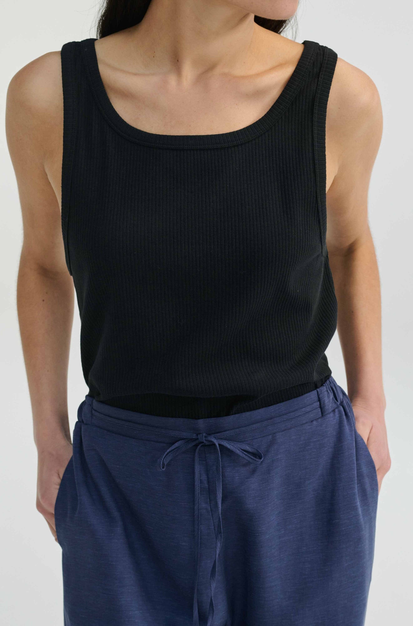 Person wearing a black tank top and blue pants on a white background